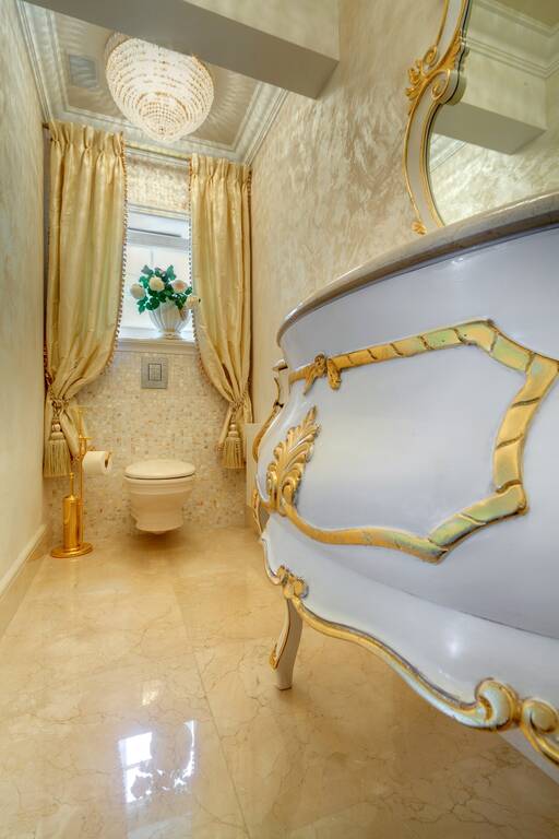 Lidia Bersani / Luxury Interior - Small classical toilet, White sink cabinet, gold decorated. Marble crema marfil on the floor and silk curtains in the windows